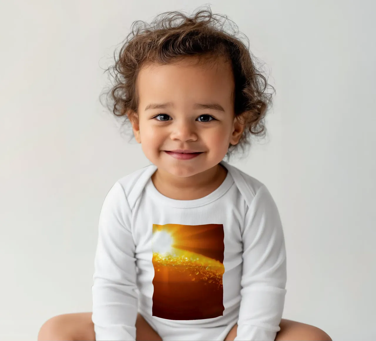 Sunlight glistens on a dewy surface at dawn, creating a warm long-sleeve baby romper by DesignDoodle
