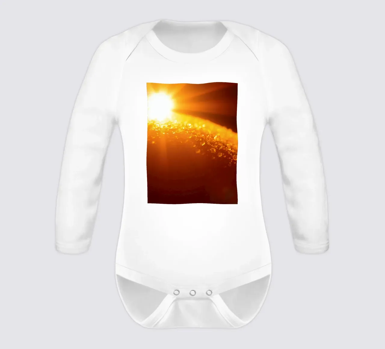Sunlight glistens on a dewy surface at dawn, creating a warm long-sleeve baby romper by DesignDoodle