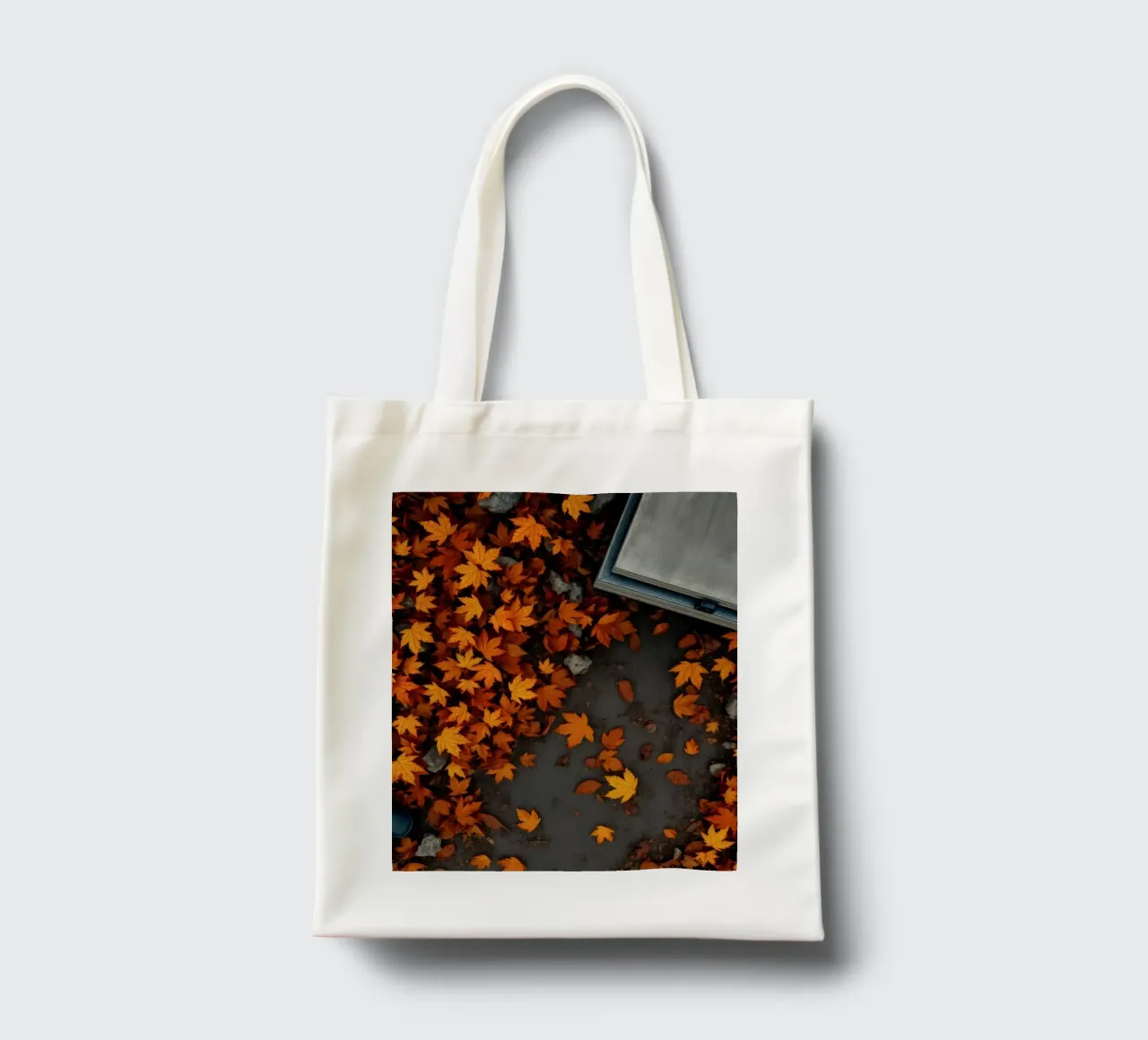 Foglie autunnali dorate si disperdono a terra vicino a un sentiero di pietra borsa in juta da DesignDoodle