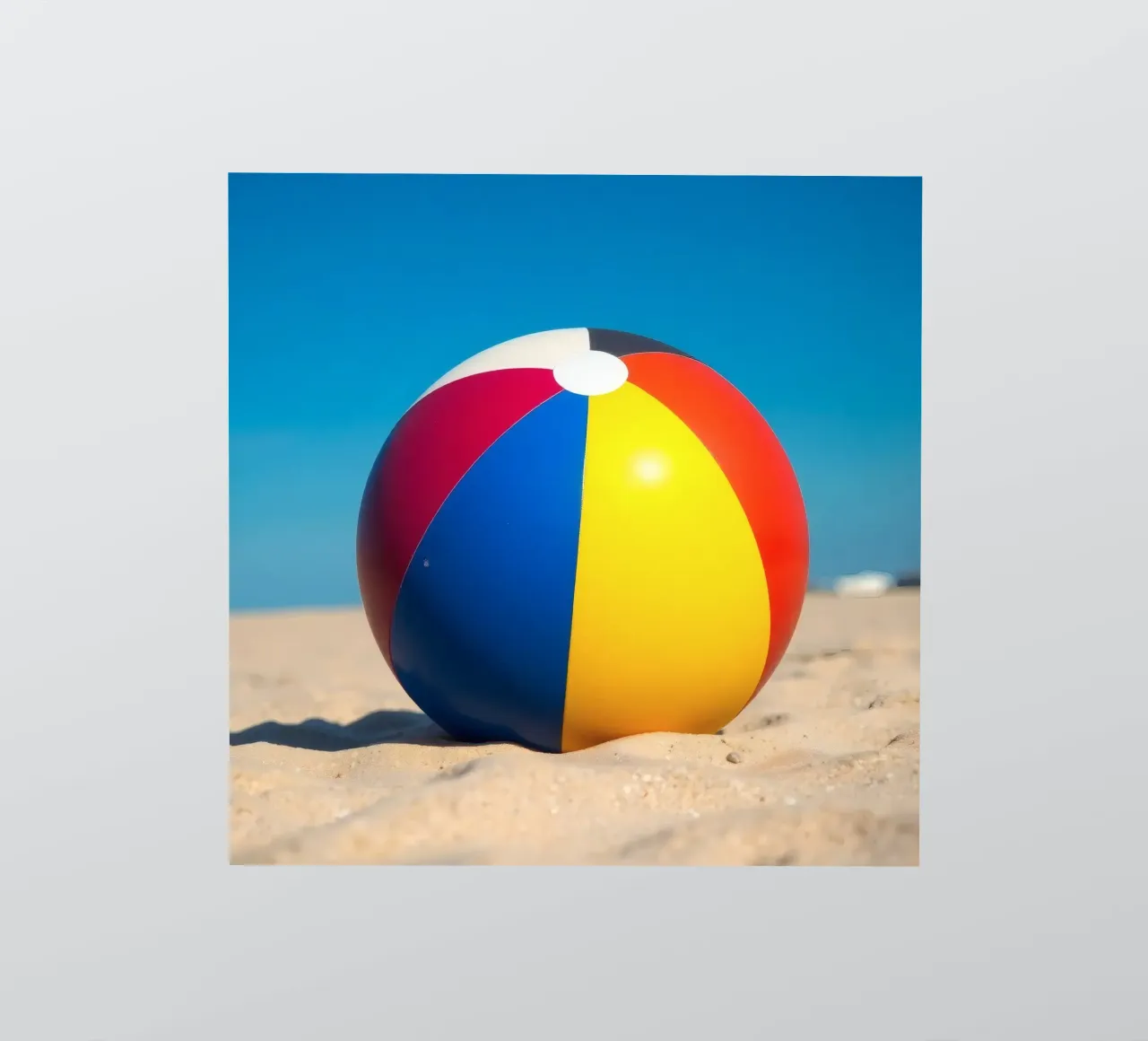 un ballon de plage est posé sur un rivage sablonneux sous un ciel bleu éclatant. autocollant de DesignDoodle