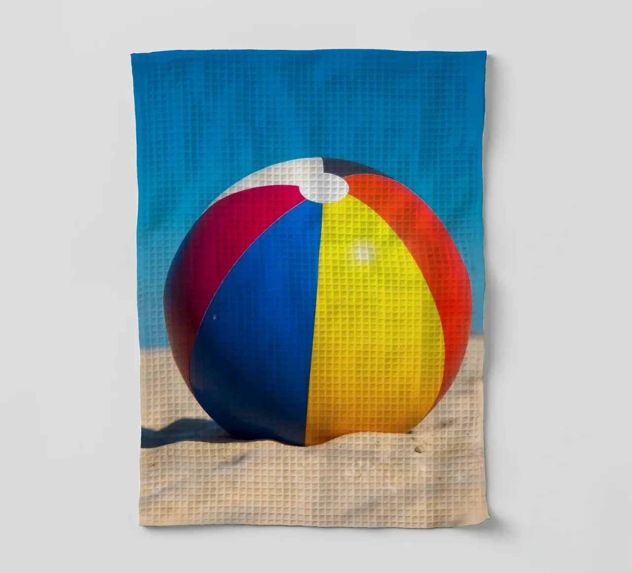 un ballon de plage est posé sur un rivage sablonneux sous un ciel bleu éclatant. torchon de DesignDoodle
