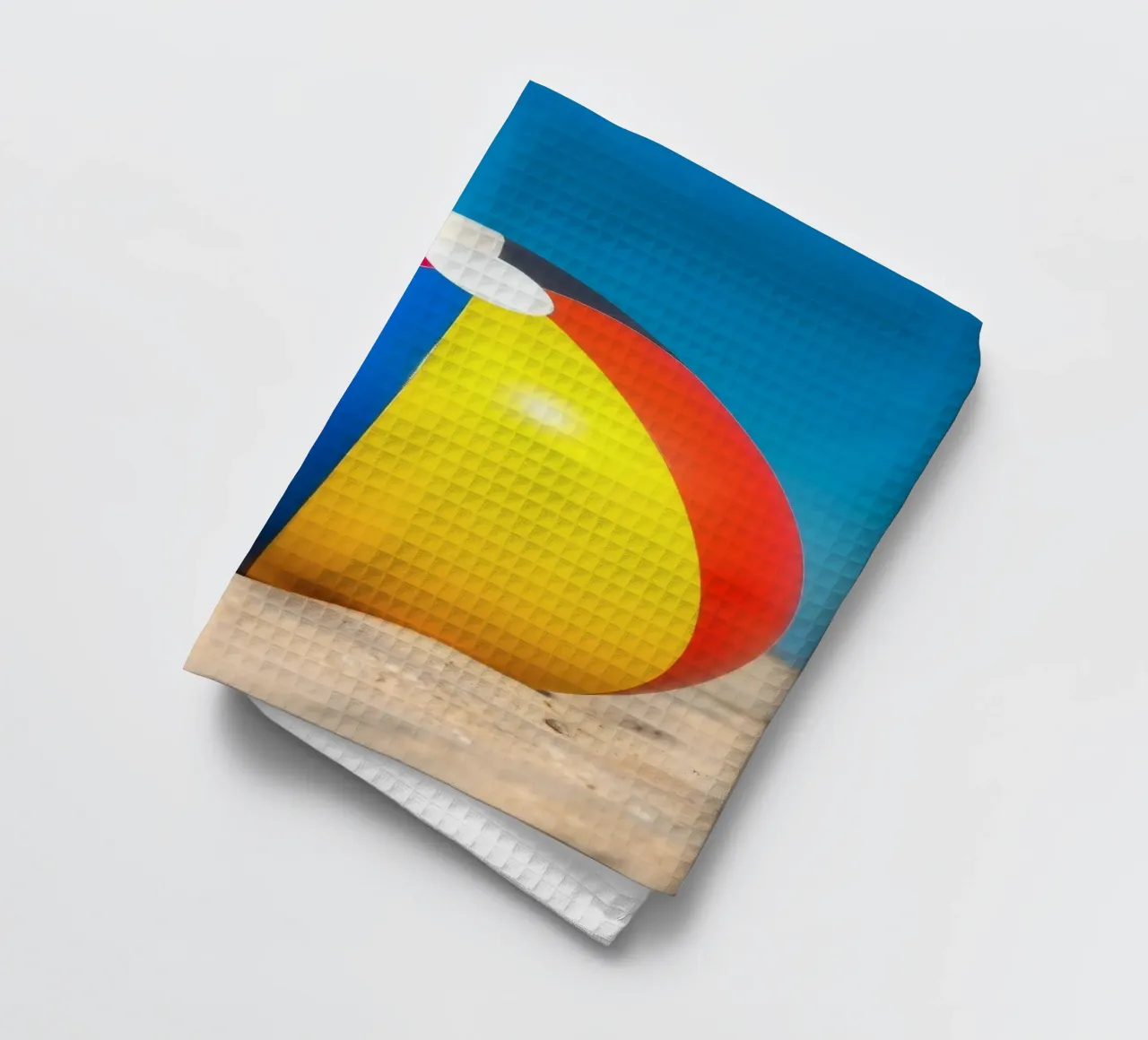 un ballon de plage est posé sur un rivage sablonneux sous un ciel bleu éclatant. torchon de DesignDoodle