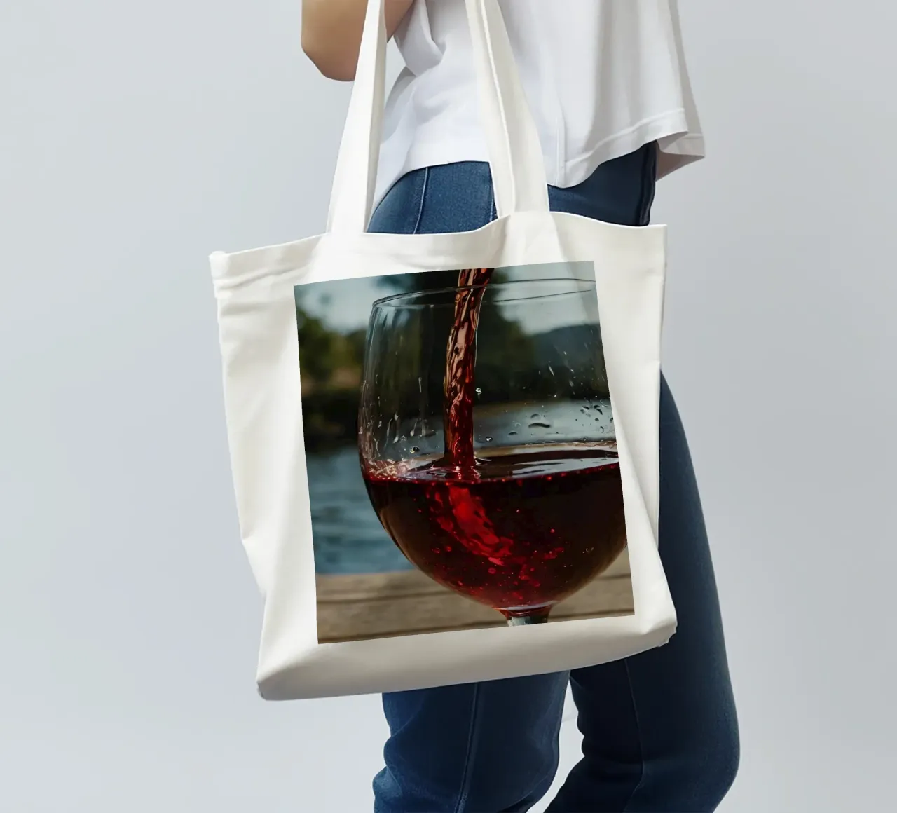 Pouring red wine into a glass beside a tranquil lake at suns tote bag by DesignDoodle