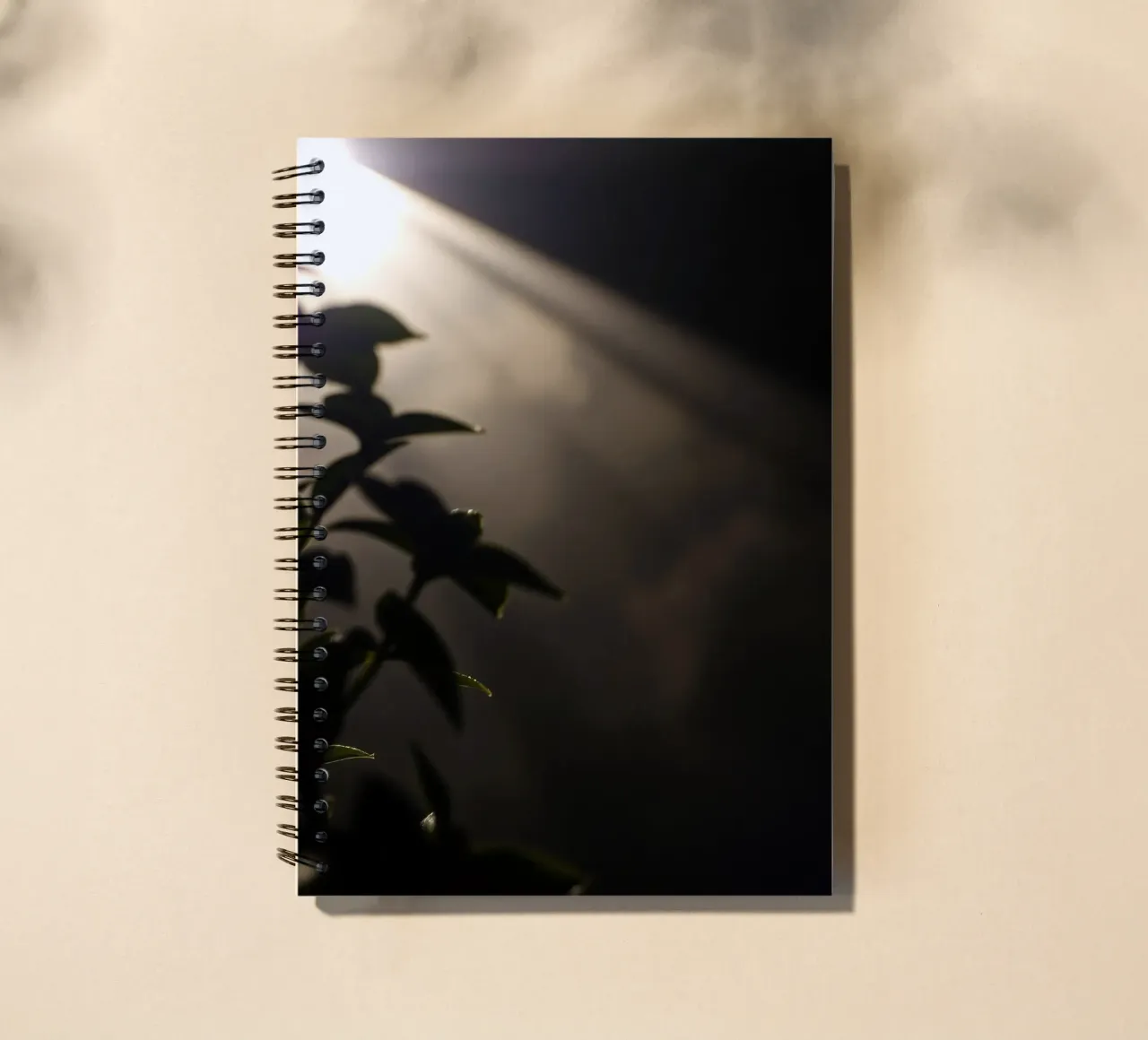 Light pierces through darkness, illuminating a plant spiral notebook by DesignDoodle