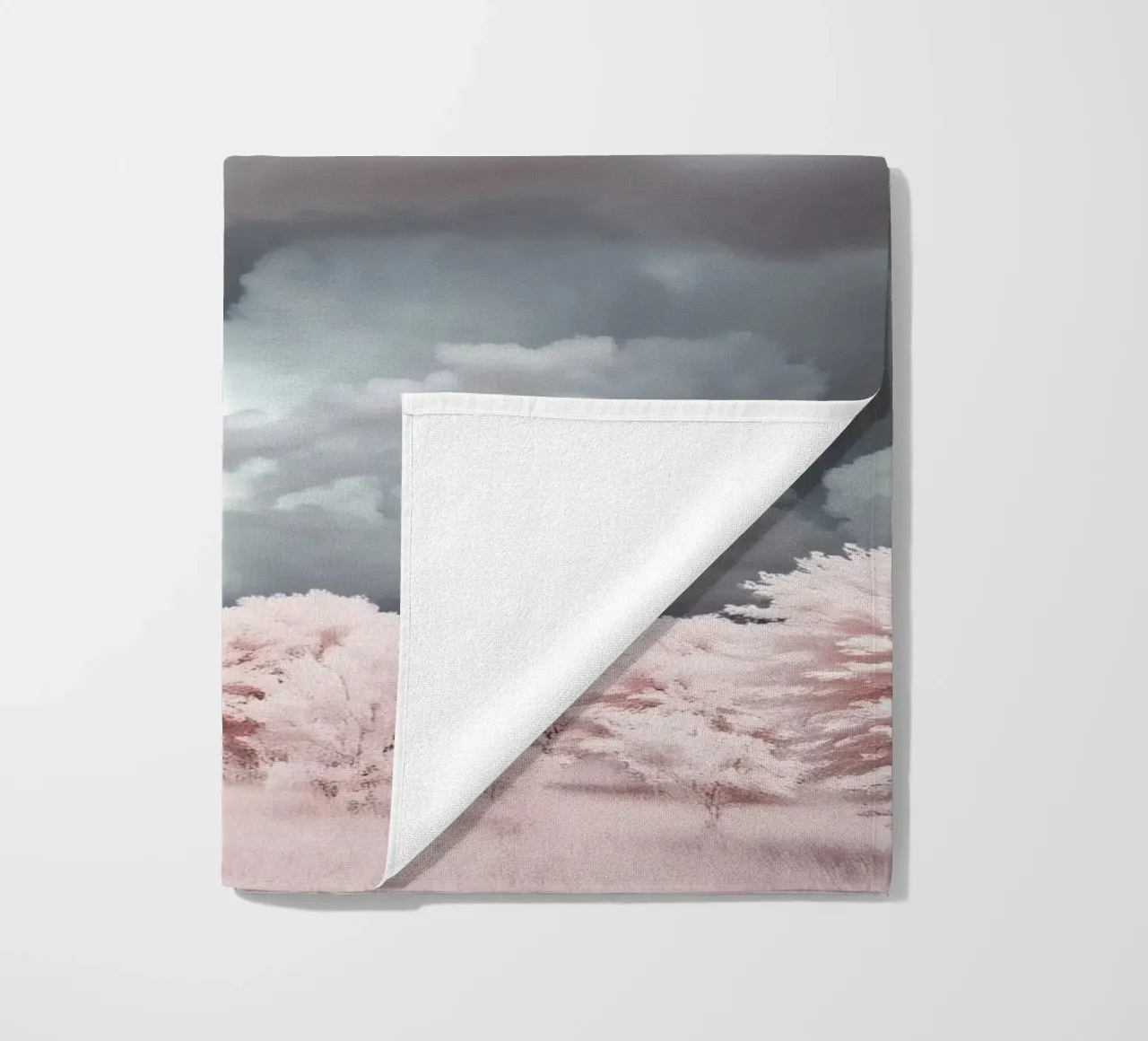 Dramatic clouds hover over pink-tinted trees in an enchantin beach towel by DesignDoodle