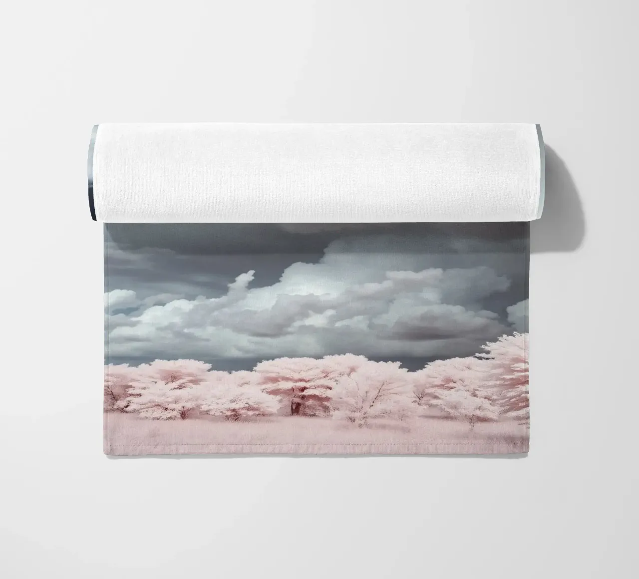 Dramatic clouds hover over pink-tinted trees in an enchantin beach towel by DesignDoodle