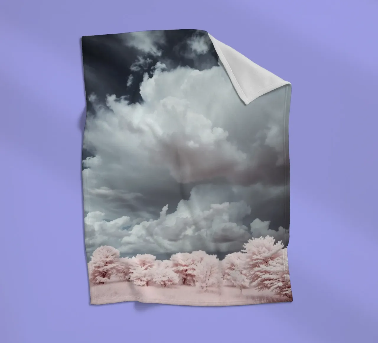 Dramatic clouds hover over pink-tinted trees in an enchantin fleece blanket by DesignDoodle