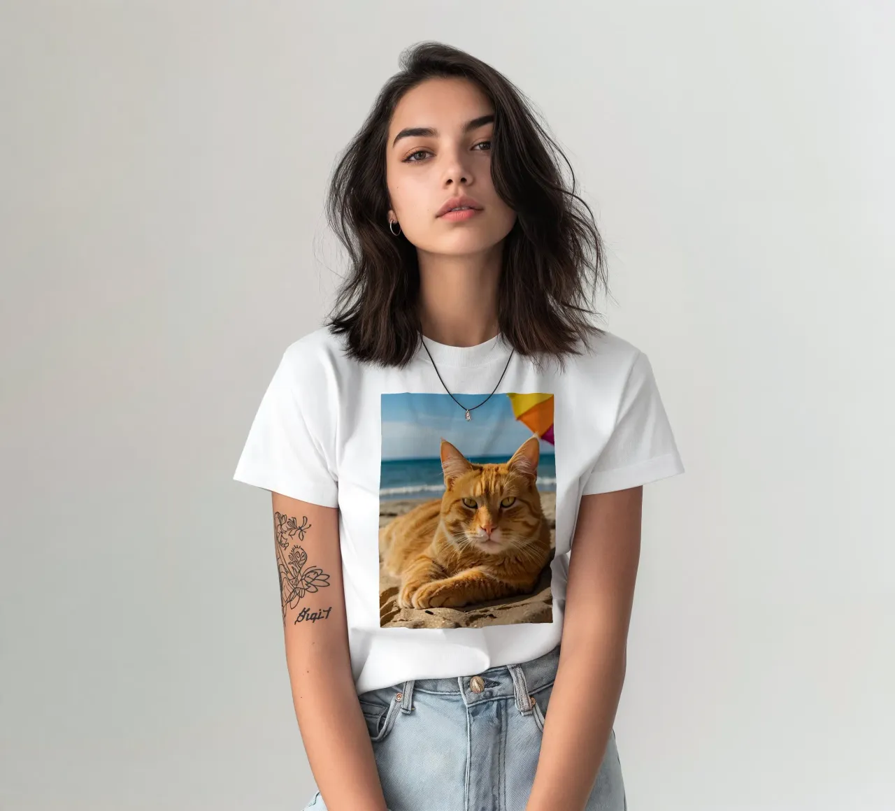 Gatto arancione che si rilassa sulla spiaggia sabbiosa sotto un ombrellone colorato t-shirt da DesignDoodle
