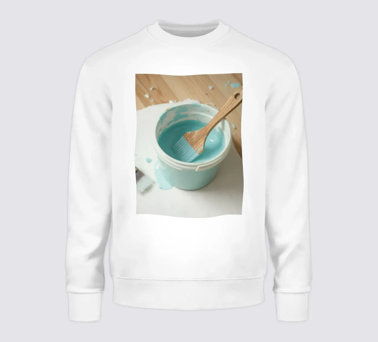 Un pincel de madera descansa en un bote de pintura azul junto a una brocha pequeña sudadera de DesignDoodle