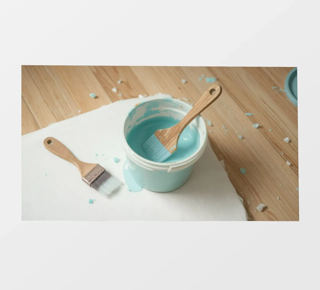 Il pennello di legno è appoggiato in un barattolo di vernice blu accanto a un pennello piccolo. telo in pvc da DesignDoodle