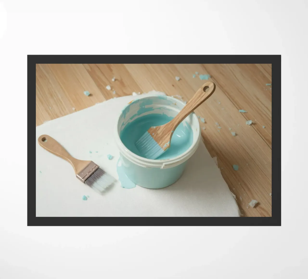 Un pincel de madera descansa en un bote de pintura azul junto a una brocha pequeña felpudo de DesignDoodle