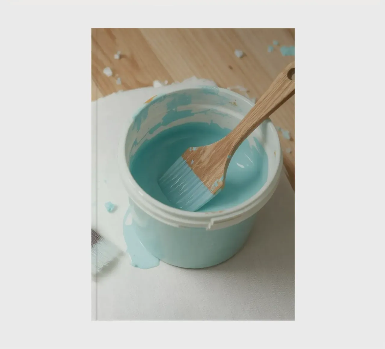 Un pinceau en bois repose dans un pot de peinture bleu à côté d'un petit pinceau. carnet de notes de DesignDoodle