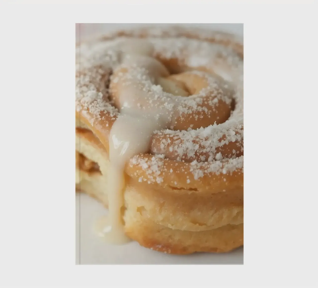 Warm cinnamon roll with cream icing and powdered sugar on a notebook by DesignDoodle