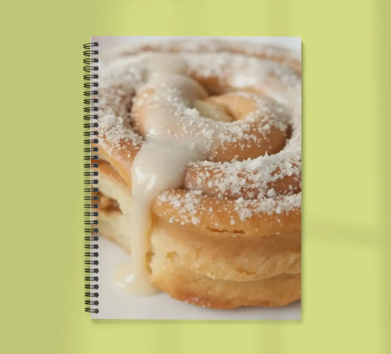 Warm cinnamon roll with cream icing and powdered sugar on a spiral notebook by DesignDoodle