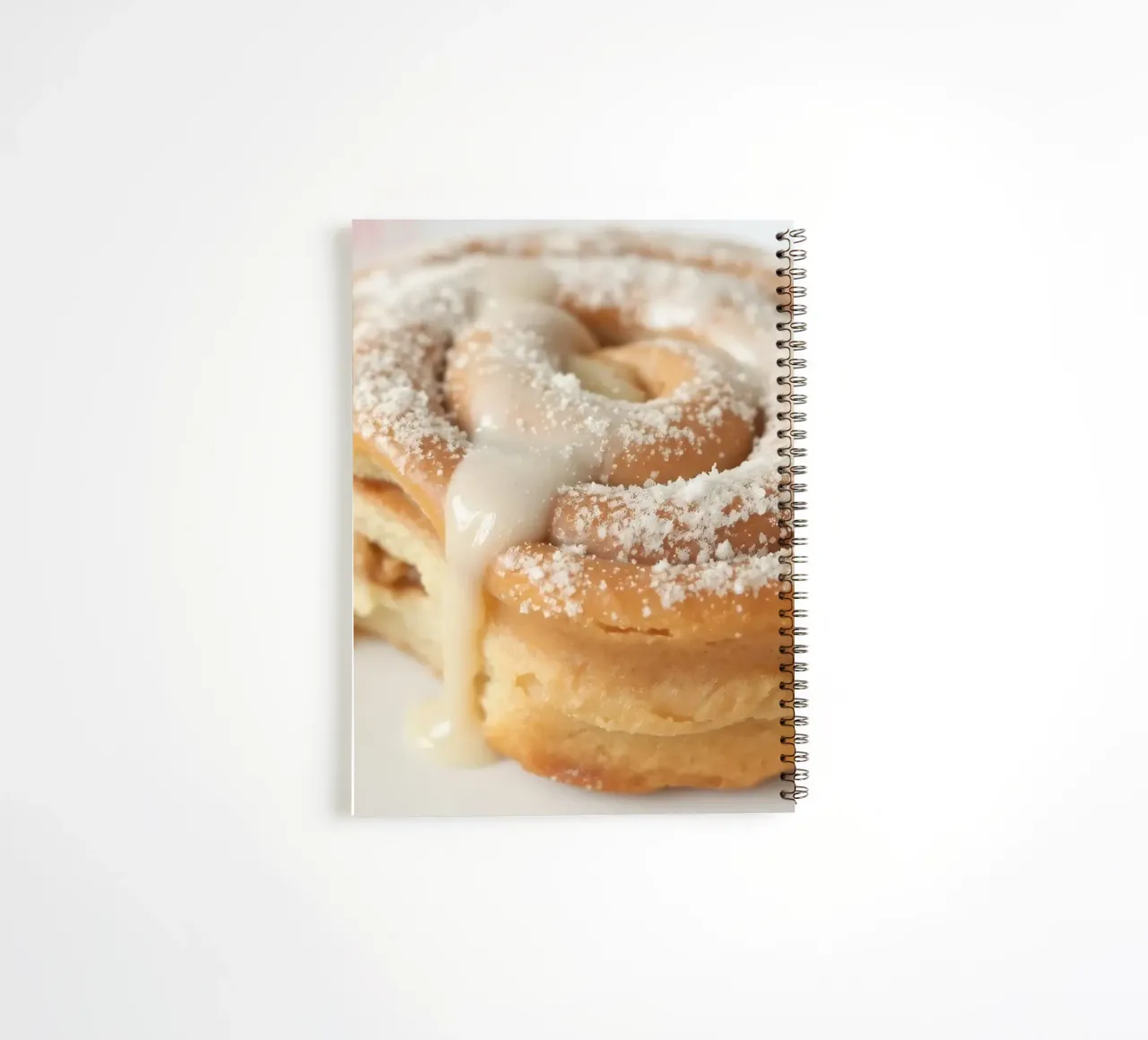 Warm cinnamon roll with cream icing and powdered sugar on a spiral notebook by DesignDoodle