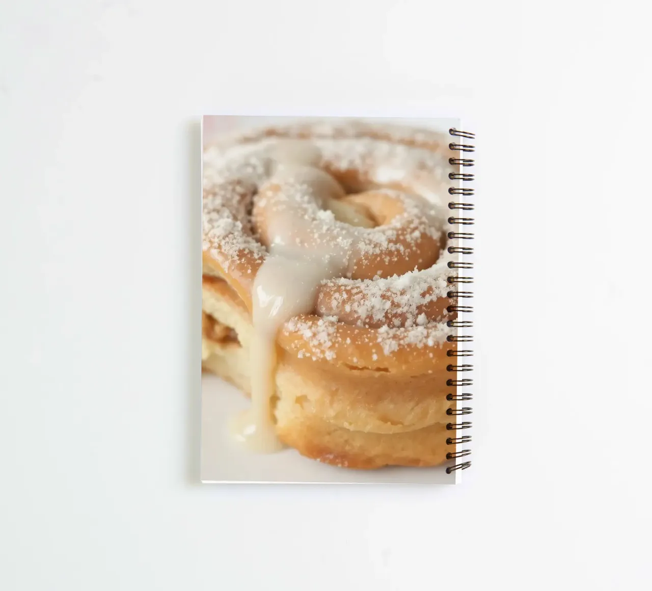 Warm cinnamon roll with cream icing and powdered sugar on a spiral notebook by DesignDoodle