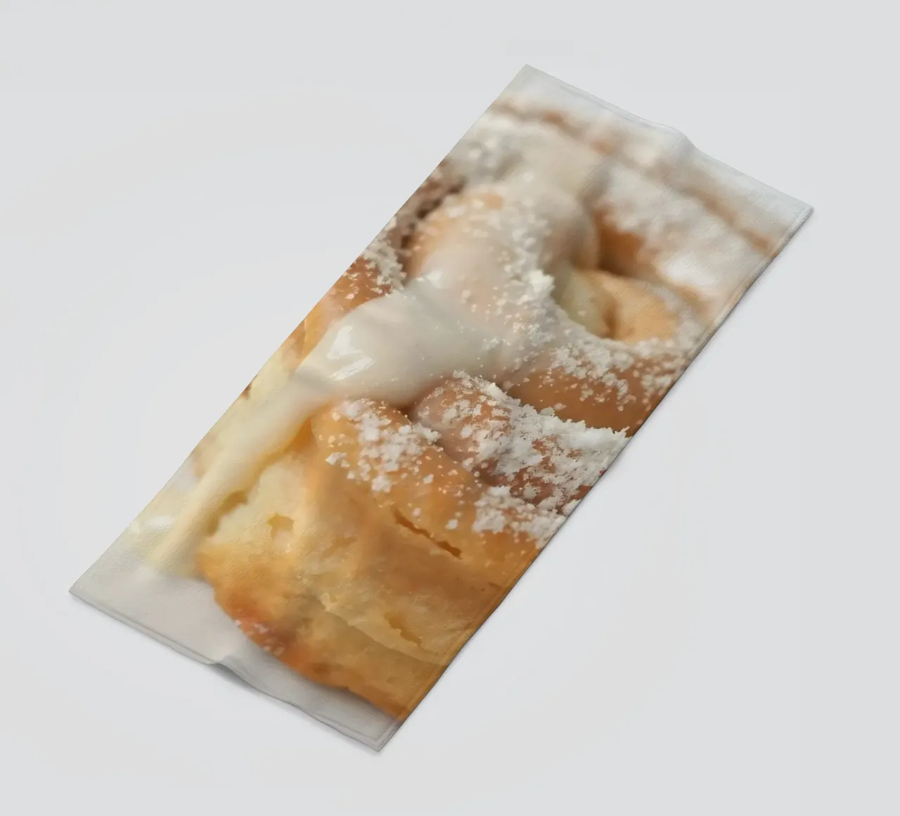 Warm cinnamon roll with cream icing and powdered sugar on a beach towel by DesignDoodle