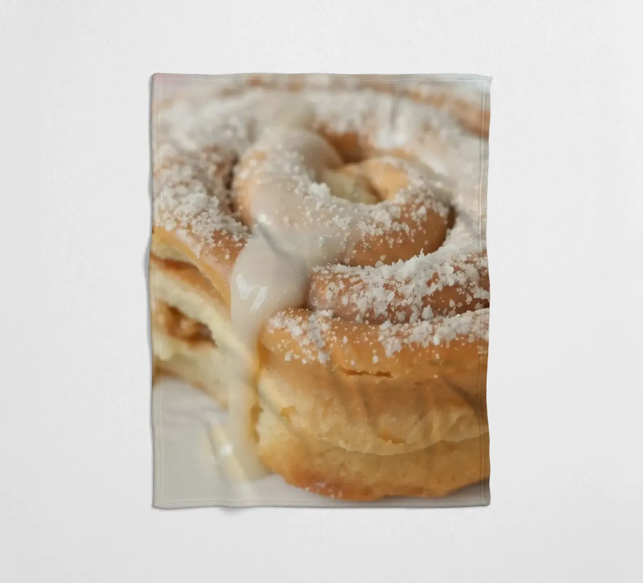 Warm cinnamon roll with cream icing and powdered sugar on a fleece blanket by DesignDoodle