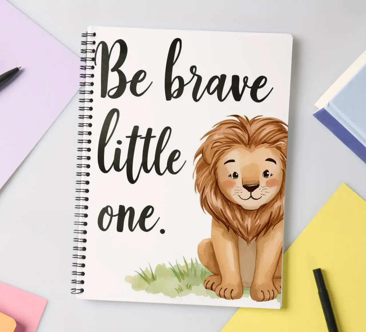 Be brave little one art with a cartoon lion sitting on grass spiral notebook by DesignDoodle