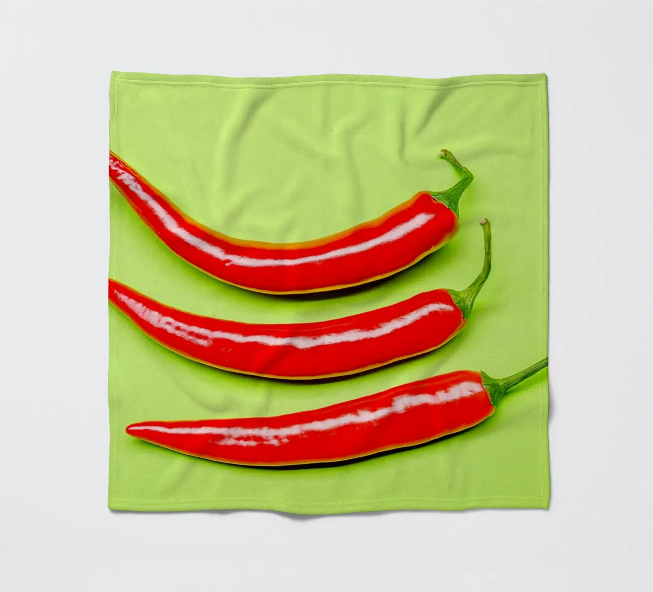 Three red chilli peppers on a green surface fleece blanket by Bilderwelt - Kunst für die Wand