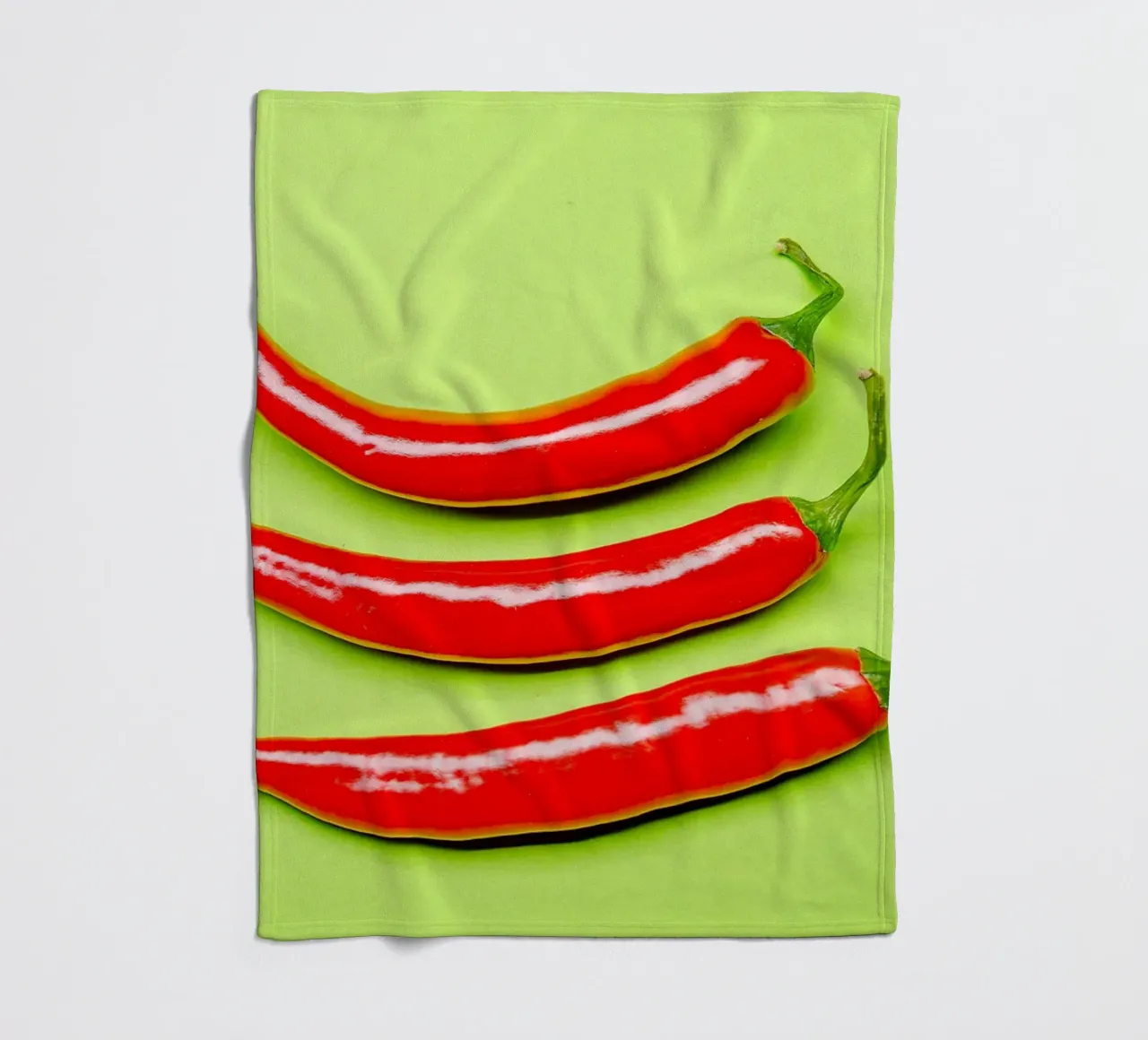 Three red chilli peppers on a green surface fleece blanket by Bilderwelt - Kunst für die Wand