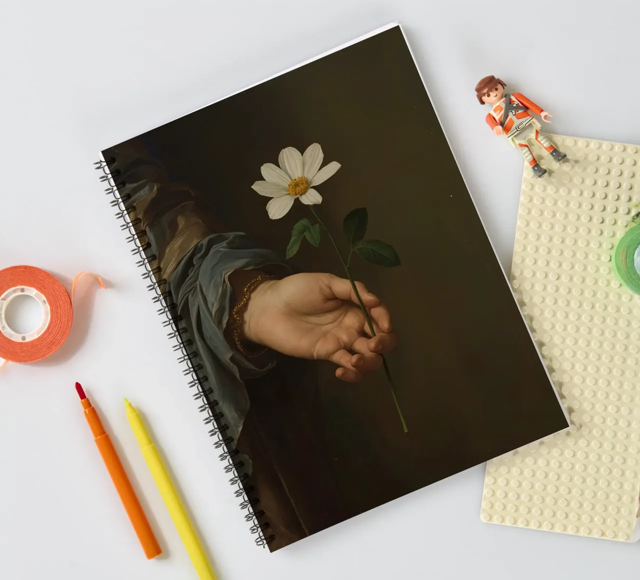 Mano che regge un fiore bianco in una luce soffusa con diario ad anelli da DesignDoodle