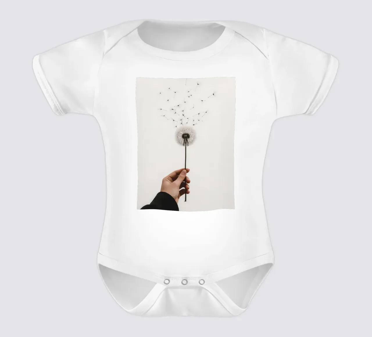 Mano que sostiene un diente de león con semillas voladoras body de bebé de DesignDoodle